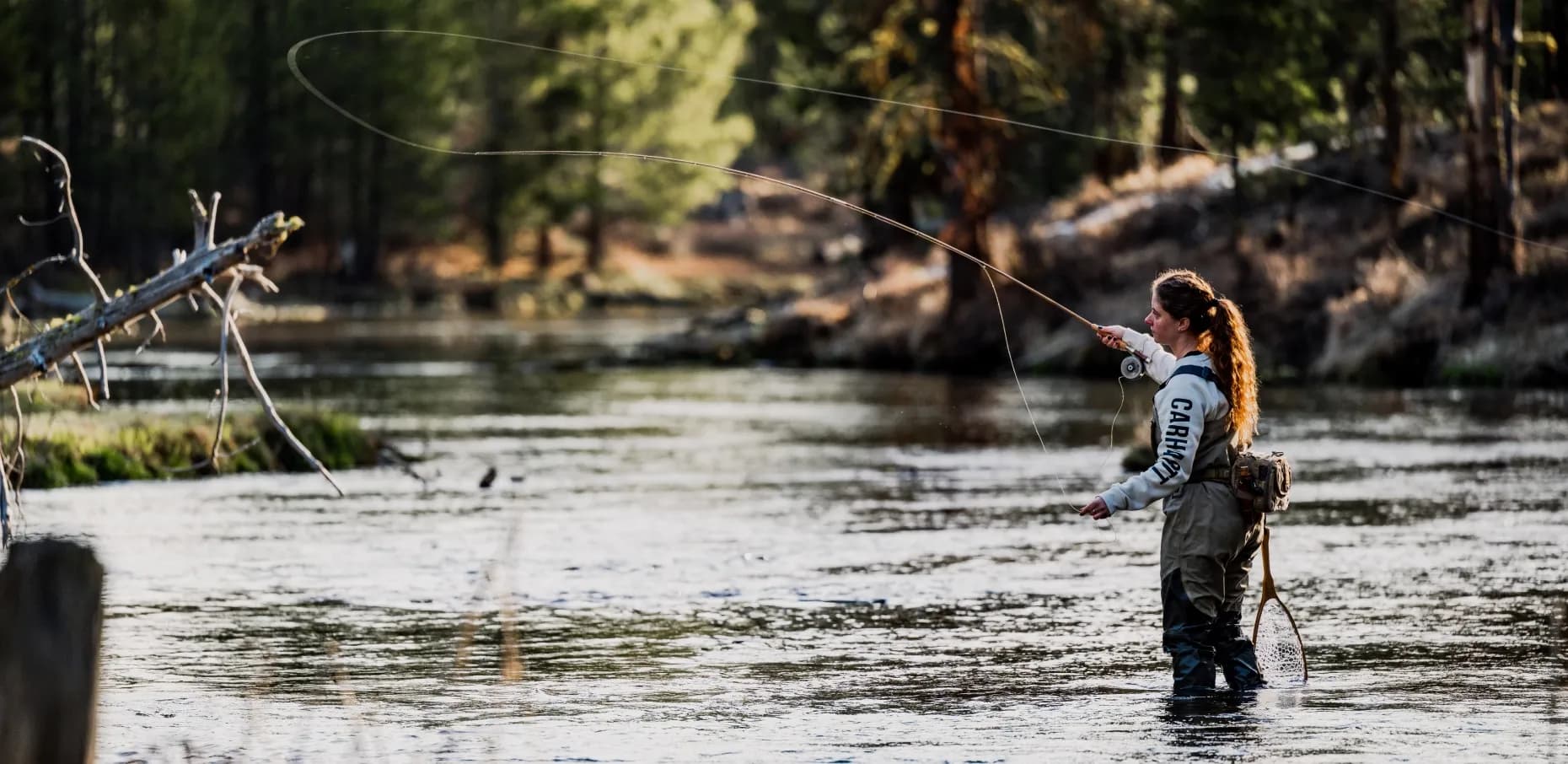 Woman fly fishing on the river wearing Carhartt